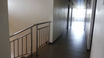 A long, narrow hallway with a metal railing on one side and a tiled floor.