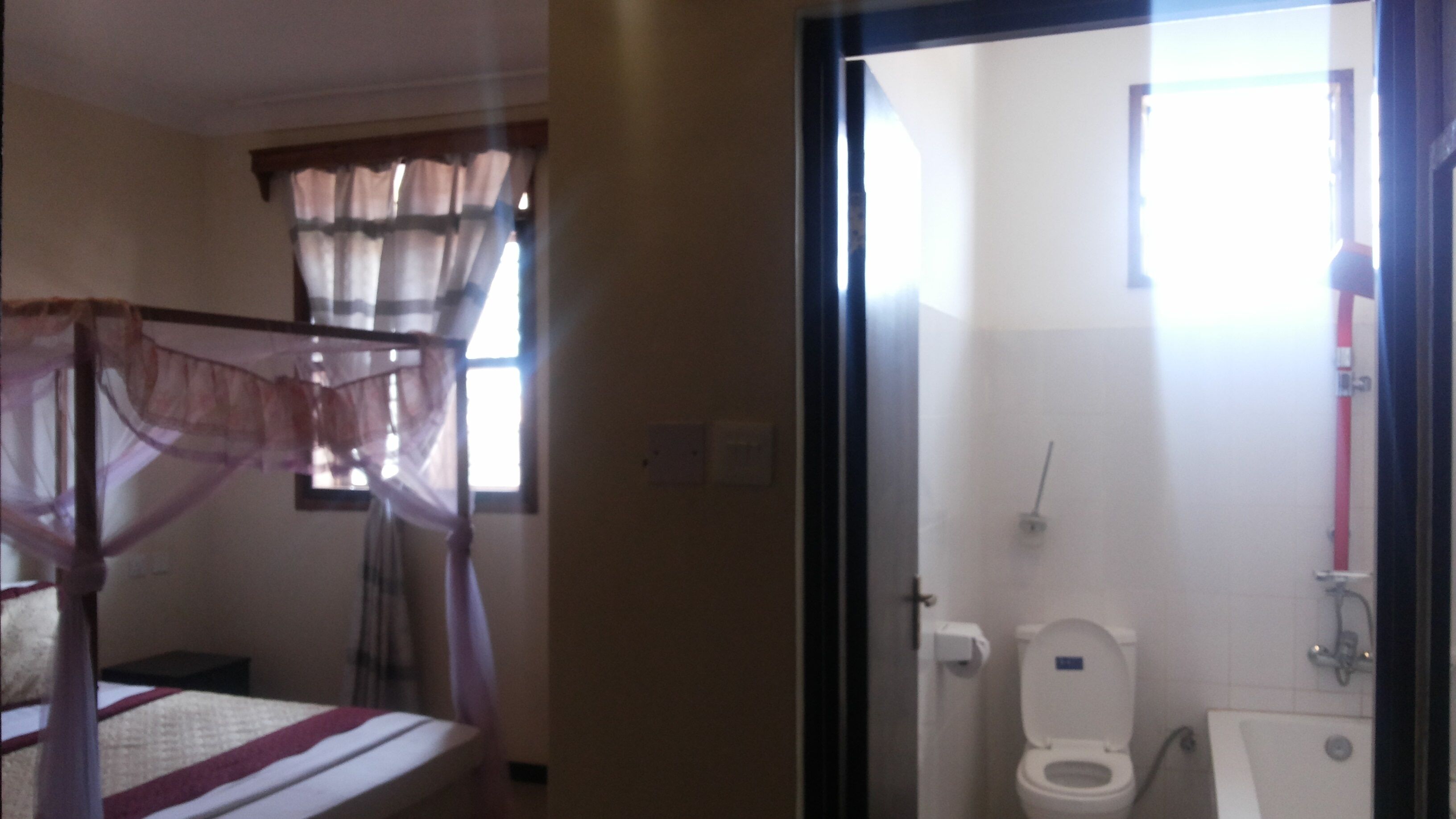 Un dormitorio con cama, ventana con cortinas y baño con inodoro y lavabo.