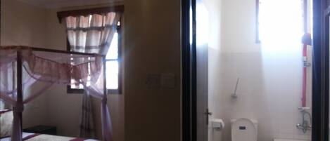 Un dormitorio con cama, ventana con cortinas y baño con inodoro y lavabo.