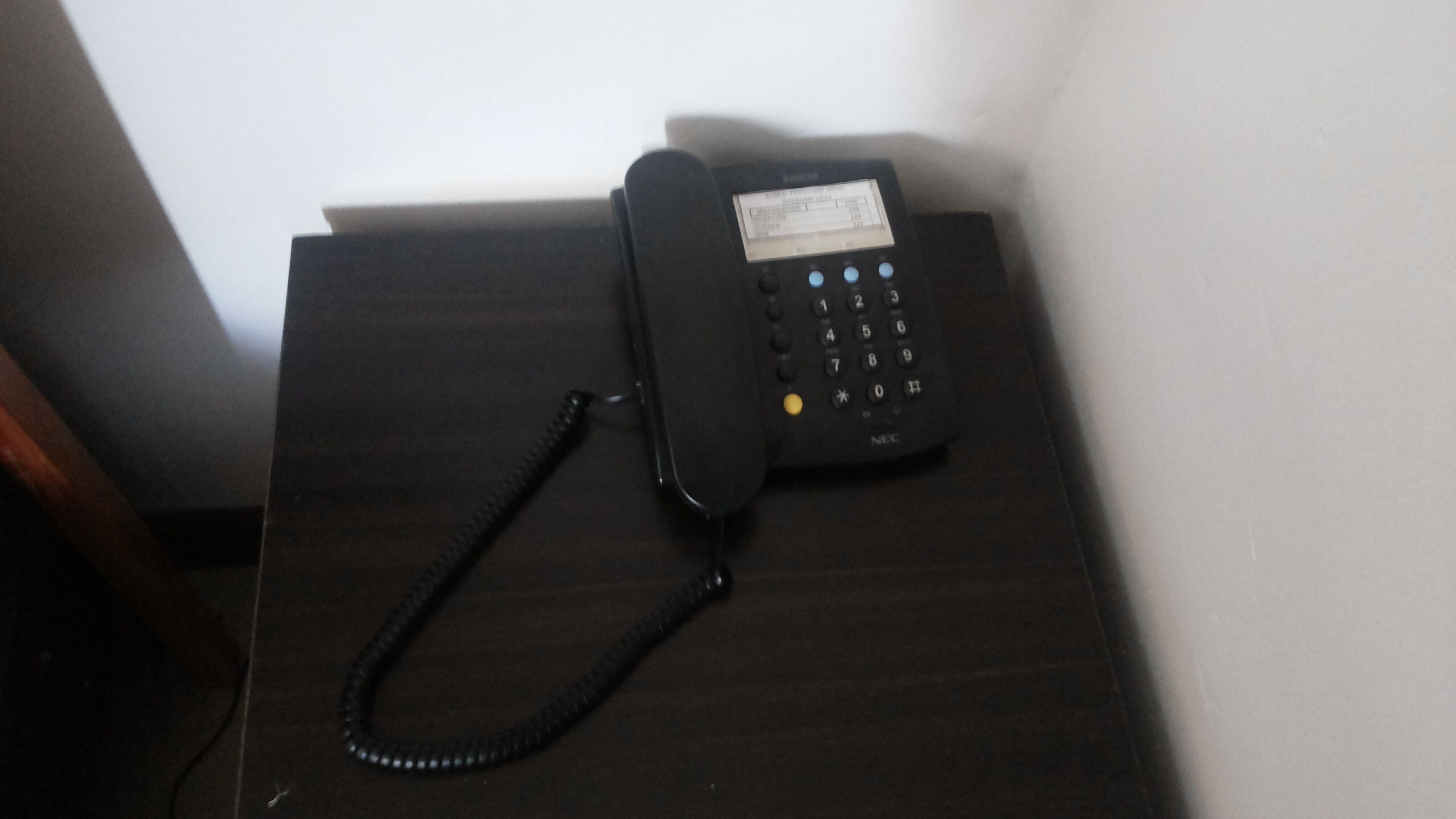 Un téléphone noir posé sur un bureau en bois foncé, avec un fil.