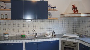 A kitchen with blue cabinets, a stainless steel sink, and a tiled backsplash. - Apartment le Maschere (Marina di Modica)