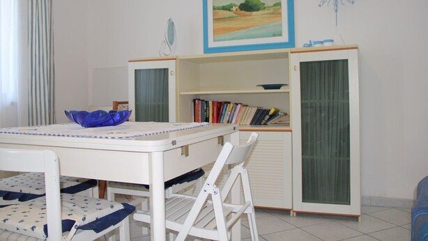 A dining area with a table, chairs, a blue bowl, a bookshelf, and a cabinet. - Apartment le Maschere (Marina di Modica)