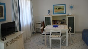 A room with a television on a cabinet, a dining table with chairs, a bookshelf, and a bed. - Apartment le Maschere (Marina di Modica)