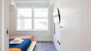 Une chambre d’hôtel étroite, avec un lit, une fenêtre et un téléviseur fixé au mur.