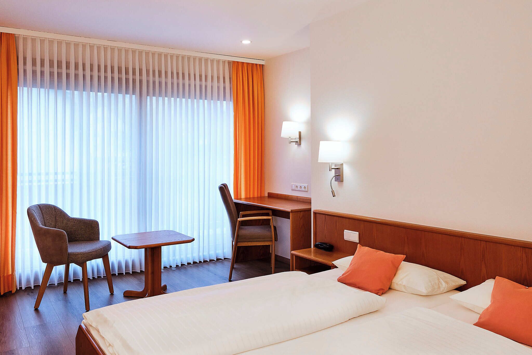 Una habitación de hotel con una cama, dos sillas, una mesita y un escritorio.