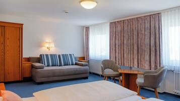 Ein Hotelzimmer mit Bett, Sofa, Sessel, Tisch und Lampe.