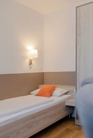 Una cama individual con cabecera de madera, una mesita de noche, una lámpara de pared y una puerta.