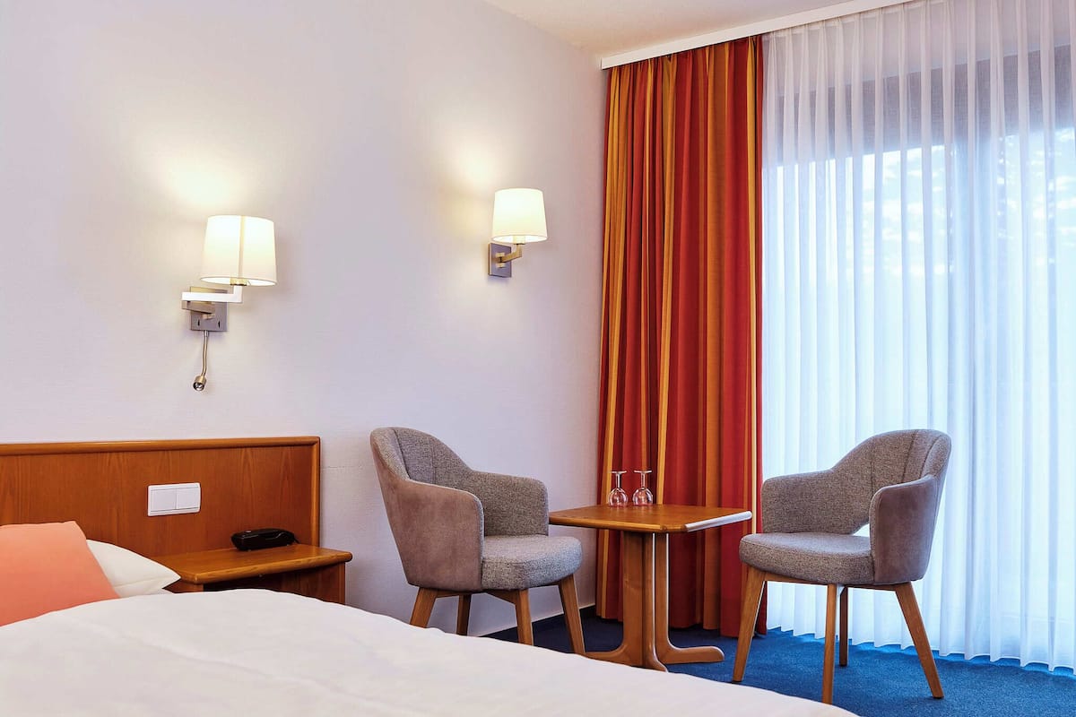 Hotellihuone, jossa on sänky, kaksi nojatuolia, pieni pöytä ja yöpöytä.