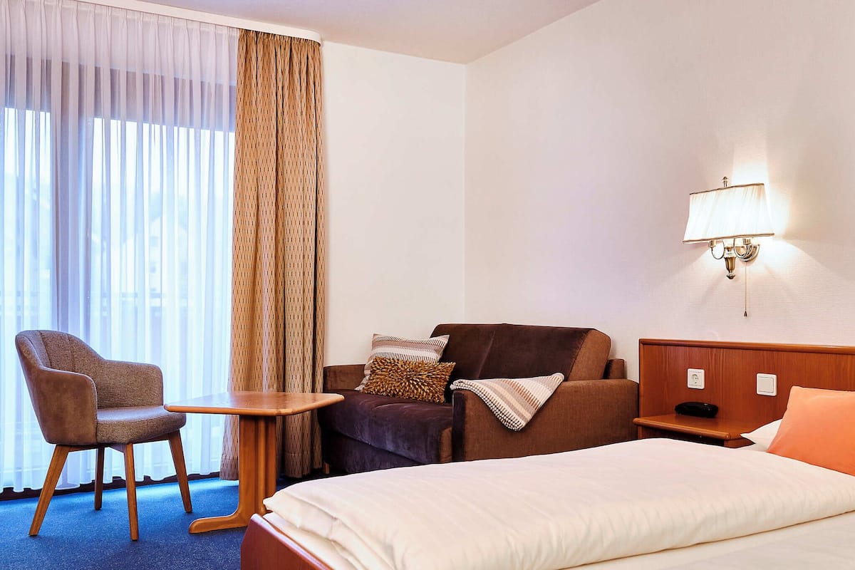 Hotellihuone, jossa on sänky, sohva, tuoli, pieni pöytä ja lamppu.