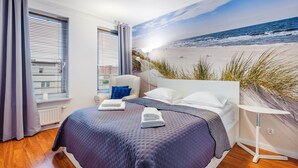 Quarto com cama, cadeira, mesa de cabeceira e um mural com tema de praia na parede.