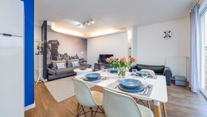 Uma sala de estar moderna com área de jantar, sofá, televisão e um mural com vista para a cidade.