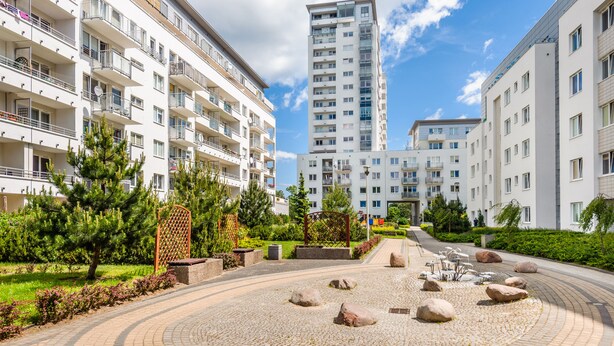 Um moderno conjunto de apartamentos com vários andares, varandas e uma área central ajardinada com pedras e plantas.