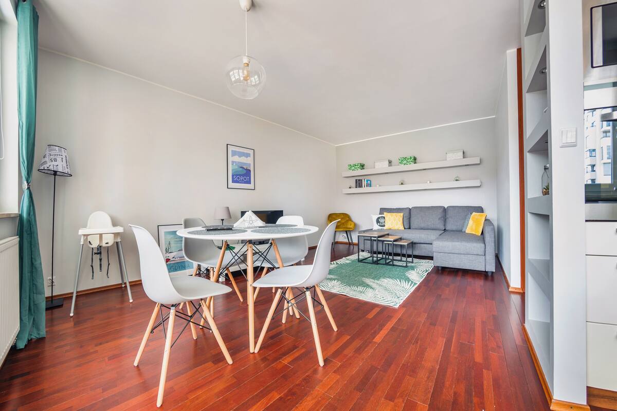 Una sala moderna con comedor, piso de madera, sofá, mesa de centro y lámpara colgante.