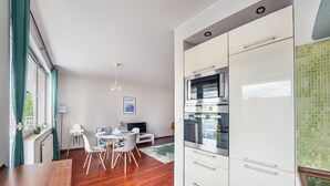 Cozinha moderna com armários brancos, forno embutido e área de refeições com mesa e cadeiras de madeira.
