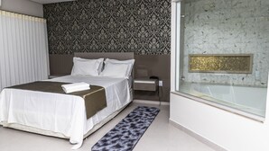Un dormitorio moderno con una cama grande, una mesita de noche, cabina de ducha con mampara de vidrio y un papel tapiz estampado.