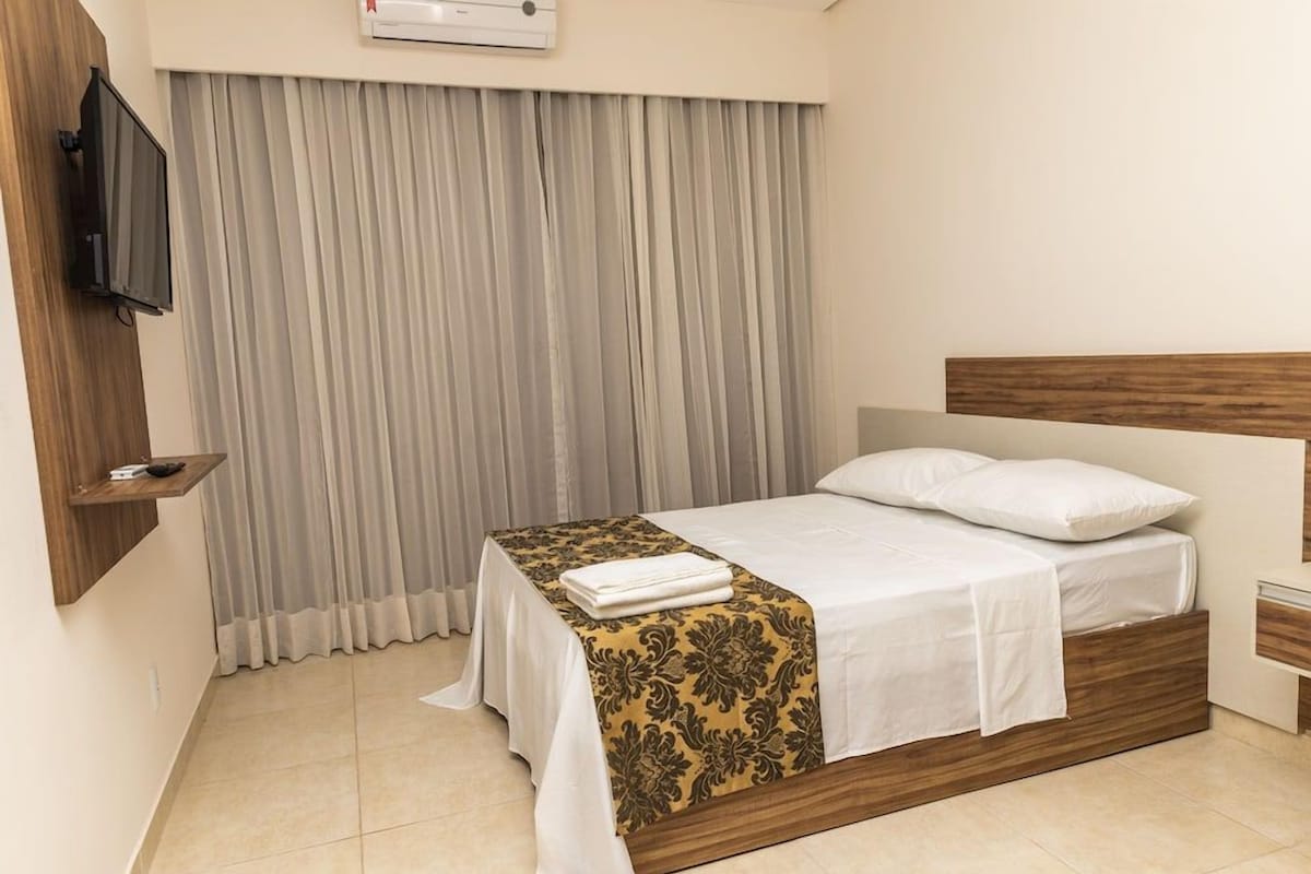Una habitación de hotel con una cama, un televisor montado en la pared y una ventana con cortinas.