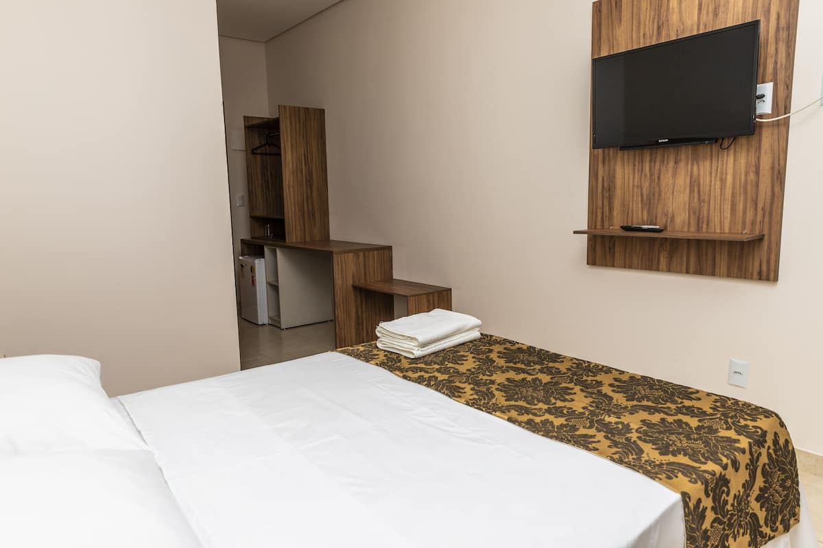 Habitación de hotel con cama, televisor montado en la pared, escritorio con silla y una mesita con control remoto.