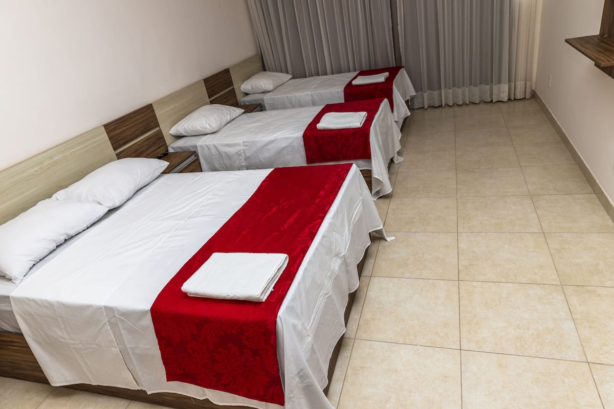 Habitación de hotel con tres camas individuales, cada una con ropa de cama blanca y detalles en rojo.