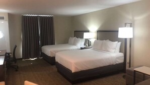 A hotel room with two beds, a desk, a chair, and a lamp.