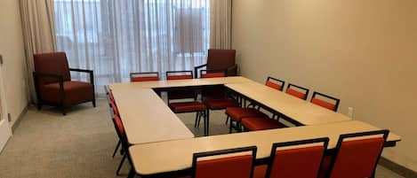 A conference room with a long table and red chairs, large windows with curtains, and a red pendant light.