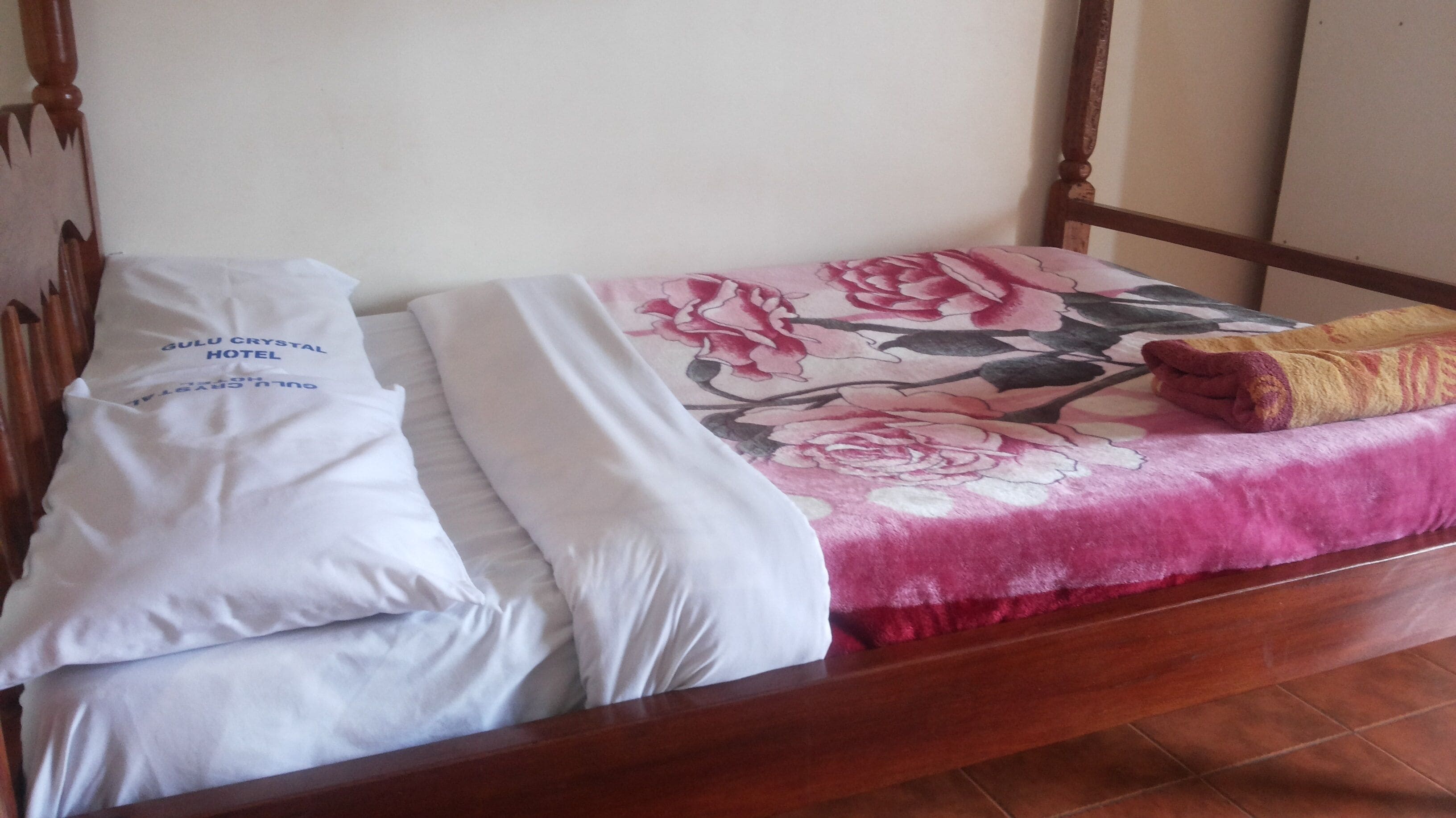 Una cama con una colcha estampada con flores, almohadas blancas y una toalla enrollada.