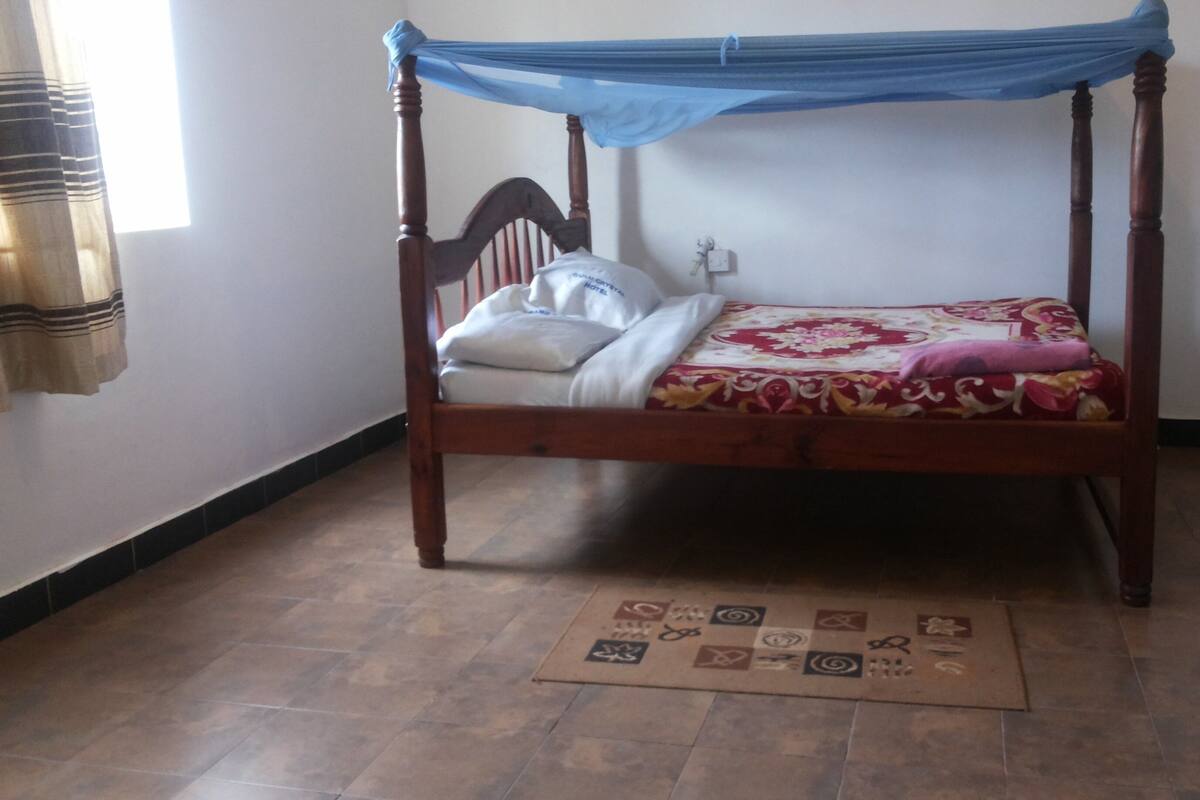 A four-poster bed with a blue canopy, a white pillow, and a floral bedspread.