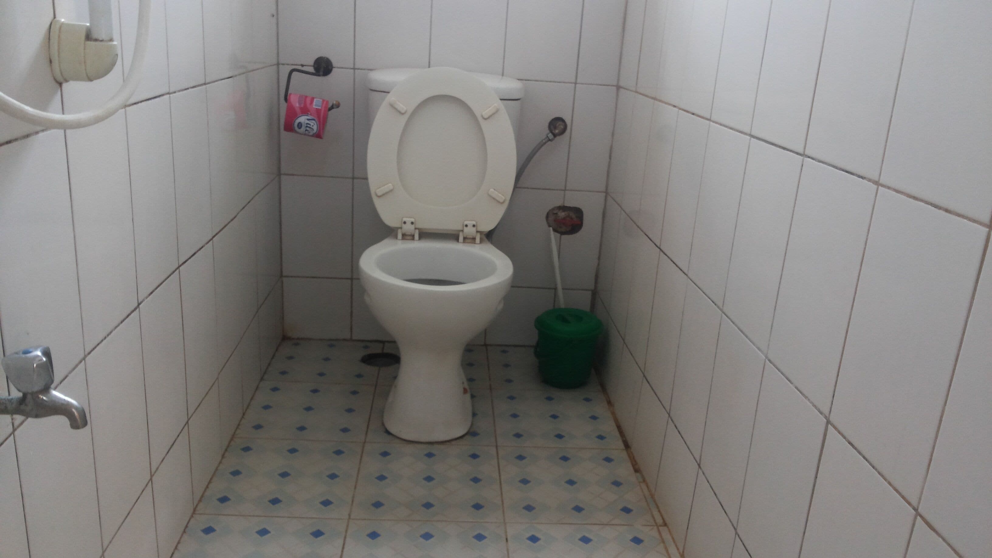 Une petite salle de bain avec des toilettes, une poubelle verte et un sèche-mains.