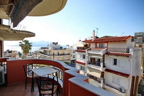 A balcony with a table and chairs overlooking a coastal cityscape with buildings and a clear sky. - Aphrodites Studios (Istiaia-Aidipsos)