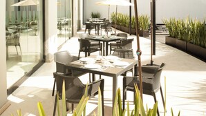 Un patio al aire libre con mesas, sillas, sombrillas y plantas en macetas.