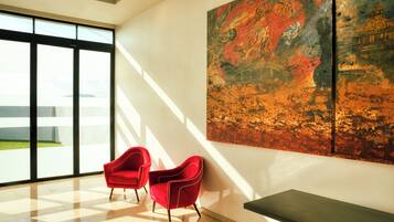 A modern interior with a large window, two red chairs, and a painting on the wall.