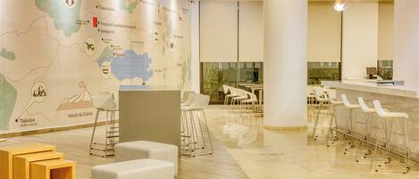 A modern hotel lobby with a large map, seating areas, and a reception desk.