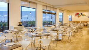 Un comedor amplio con varias mesas y sillas, ventanas grandes que ofrecen vistas al exterior, y una pared decorada con platos coloridos.