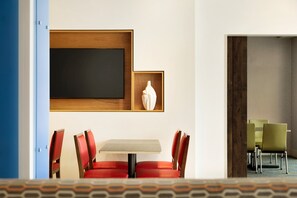 Een hotelkamer met een eethoek, inclusief een tafel en stoelen, een groot kunstwerk in een lijst aan de muur, en een vaas op een plank.