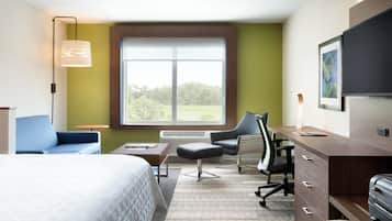 A hotel room with a bed, a desk, a chair, a lamp, and a large window.