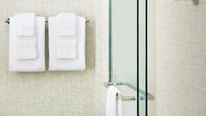 Un baño con pared de diseño geométrico, mampara de ducha de vidrio y dos toallas blancas colgadas en un perchero.