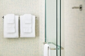 Un baño con pared de diseño geométrico, mampara de ducha de vidrio y dos toallas blancas colgadas en un perchero.