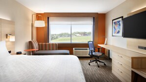 Habitación de hotel con una cama grande, un escritorio, una silla, un televisor y una ventana con vistas al exterior.