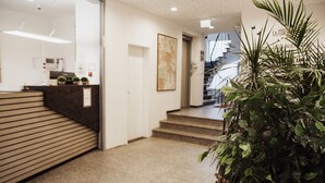 Een receptie met een receptiebalie, een trap en een grote kamerplant.