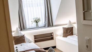A hotel room with a bed, a desk, a chair, a window with curtains, and a small table with a vase of flowers.