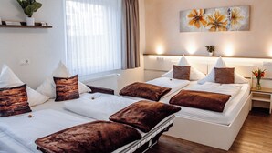 Een hotelkamer met twee bedden, elk met bruin-wit beddengoed, een groot raam met dunne gordijnen, een aan de muur bevestigd kunstwerk en een kleine plant op een plank.