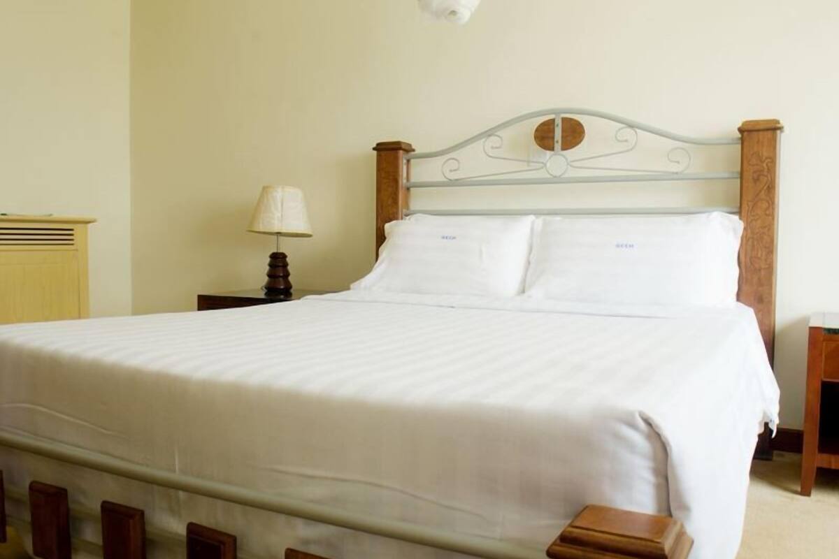 Een net opgemaakt bed met een houten hoofdbord, een bedlampje en een nachtkastje van hout.