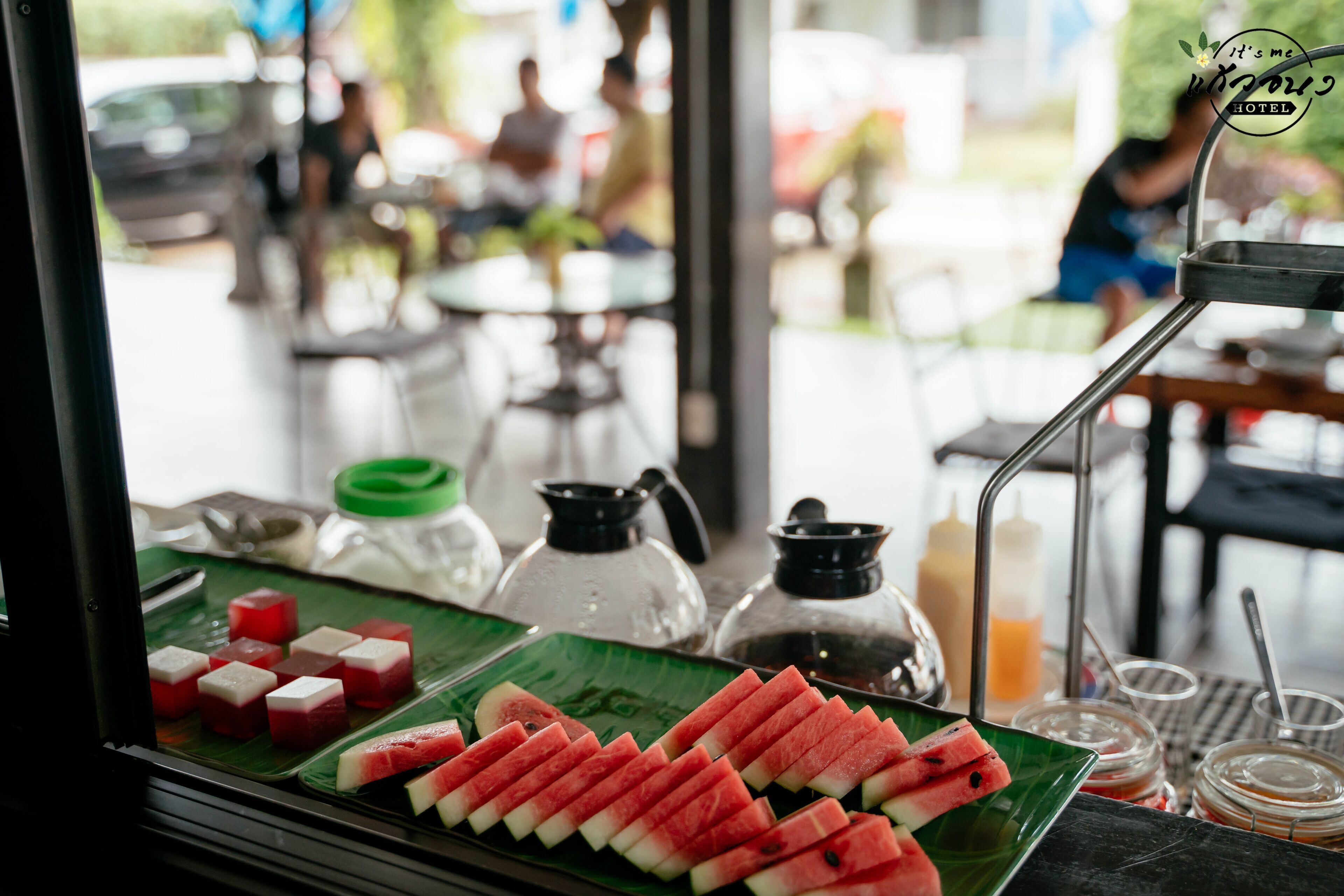 Une table avec des tranches de pastèque et une assiette verte, une cafetière et un distributeur d’eau.