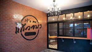 A hotel interior with a brick wall, a sign reading "It's me HOTEL", a chandelier, and a window with a view of the outside. - It's me Keawanong Hotel (Nakhon Ratchasima)
