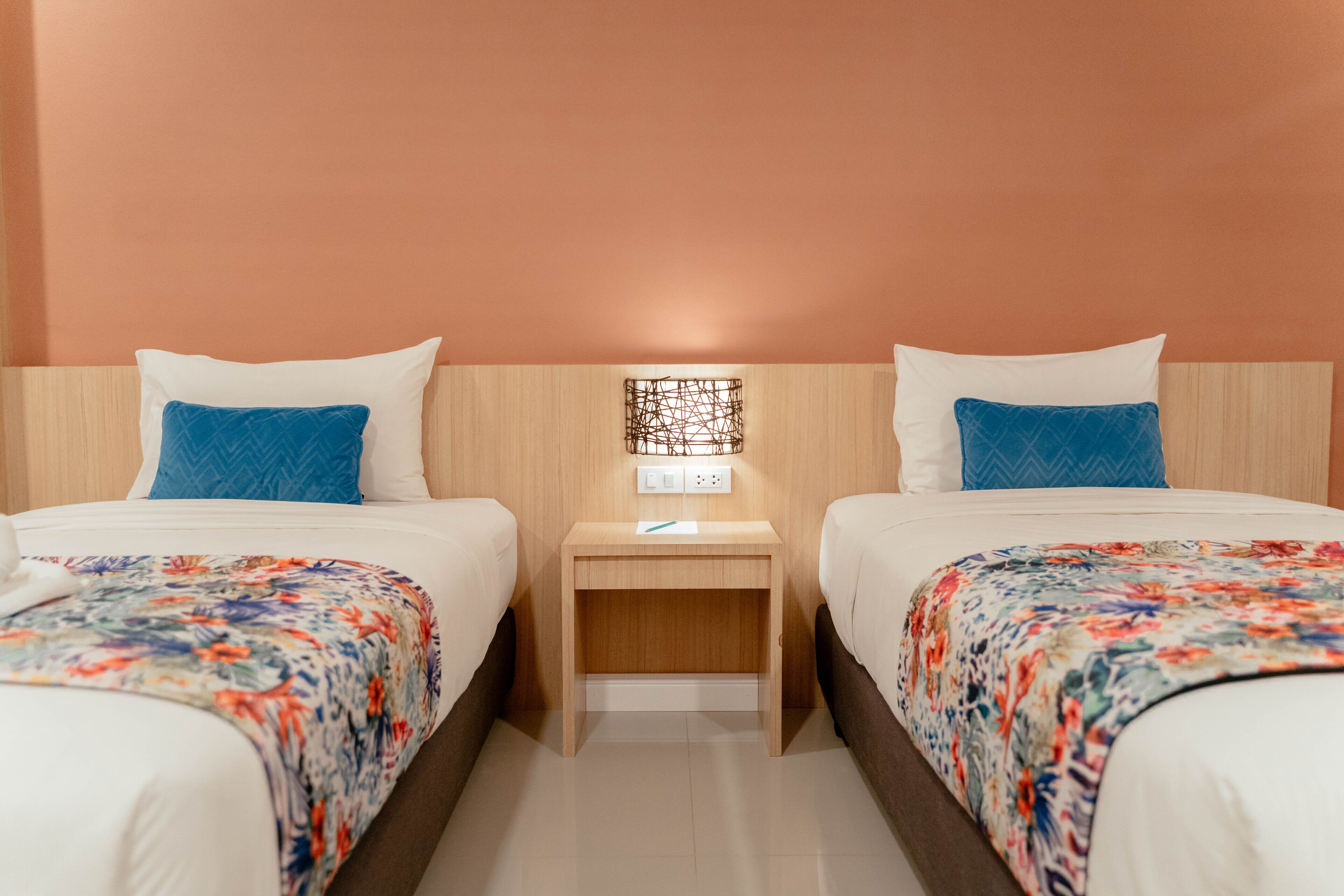 A hotel room with two beds, each with a floral bedspread, a wooden headboard, and a nightstand with a lamp between the beds.