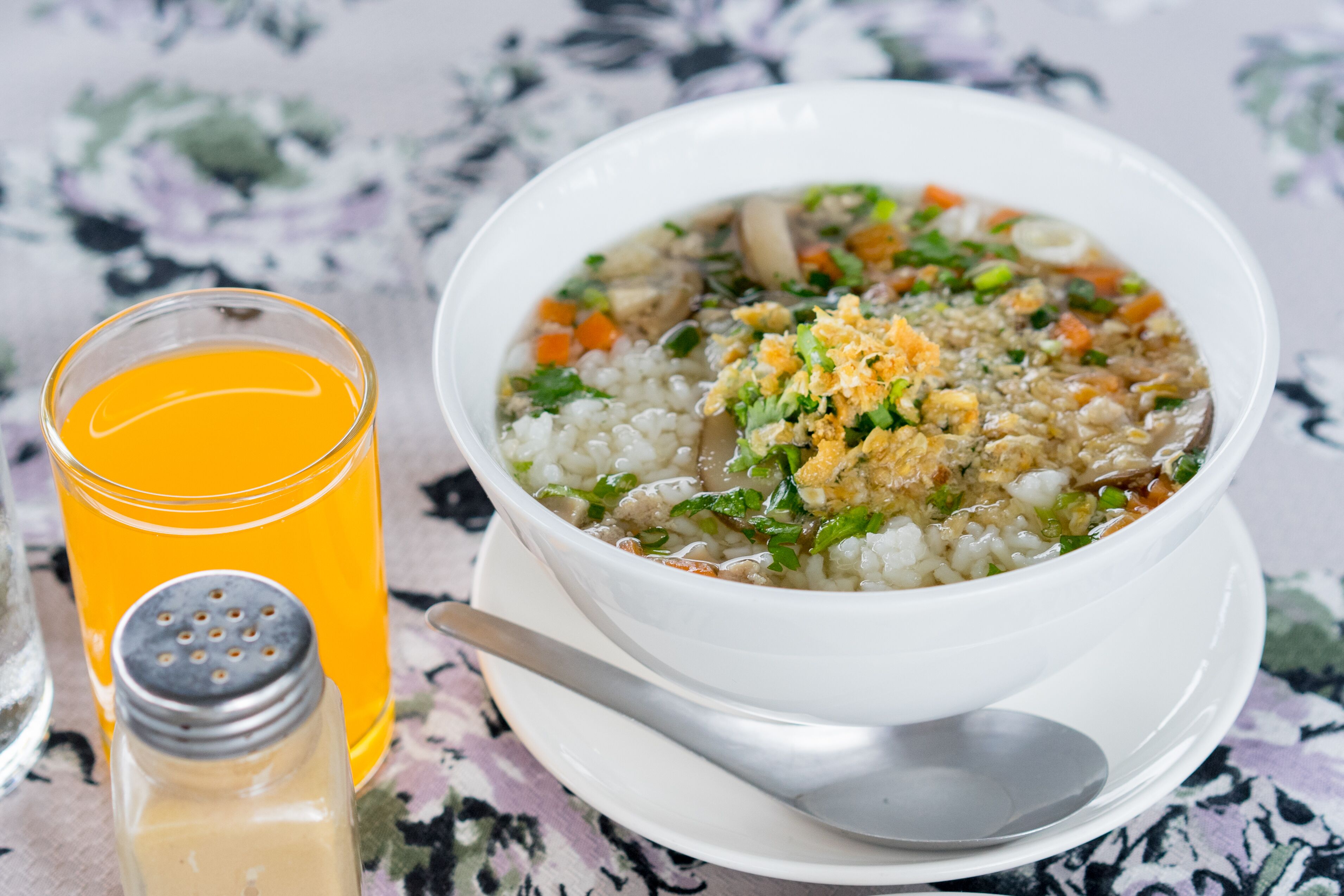 Un tazón de sopa con una cuchara y un vaso de jugo de naranja sobre una mesa.