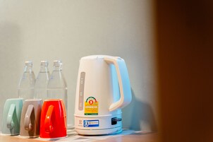 A white coffee maker with a control panel and a label, next to four colored mugs.