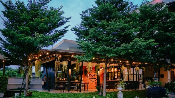 An outdoor cafe with hanging plants and string lights, surrounded by trees and a well-maintained lawn. - It's me Keawanong Hotel (Nakhon Ratchasima)