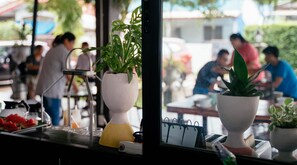 Interior de un restaurante con plantas en macetas, un panel con la carta y vistas a la calle.