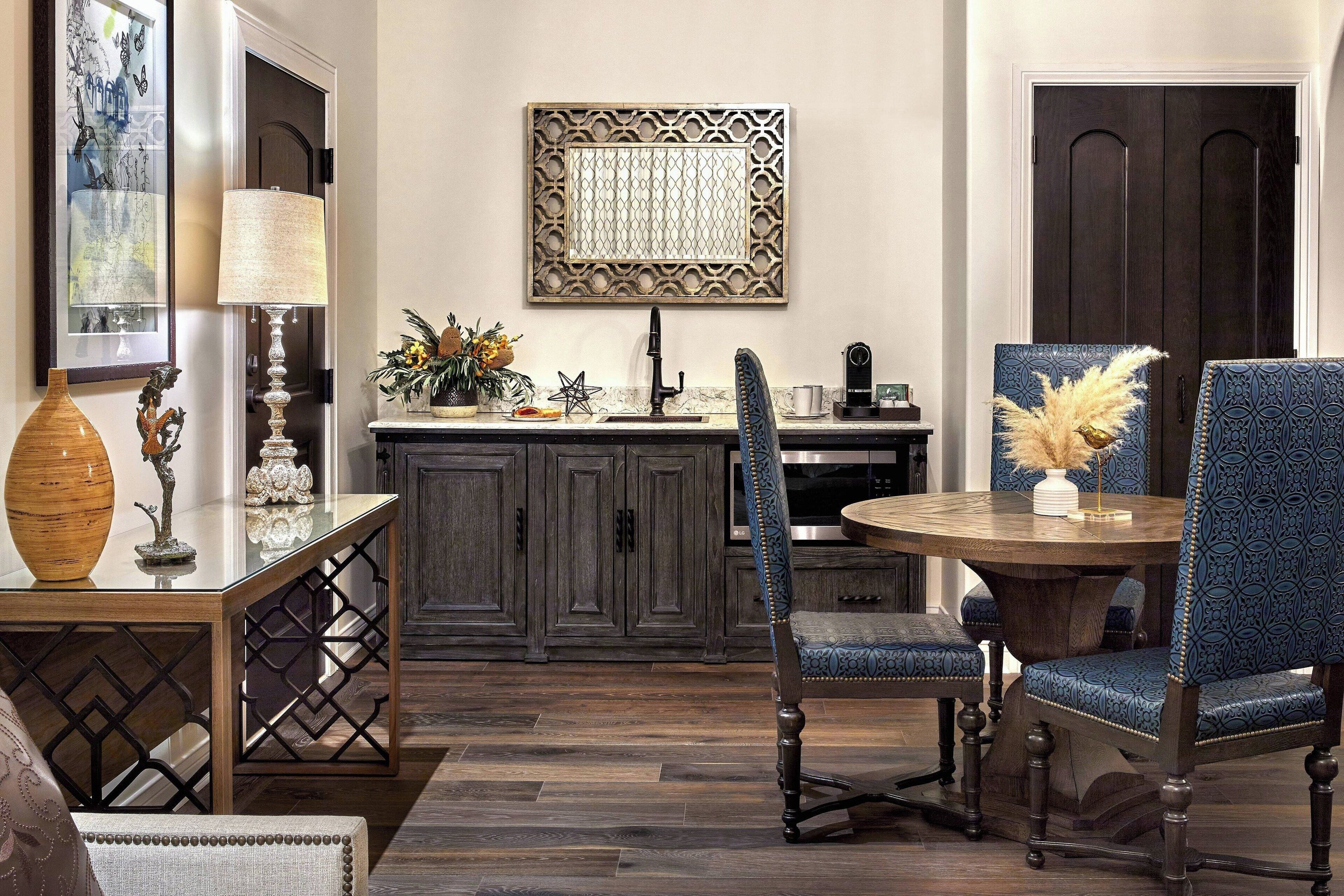 A dining area with a round table, two blue upholstered chairs, a decorative vase, and a wall-mounted artwork.
