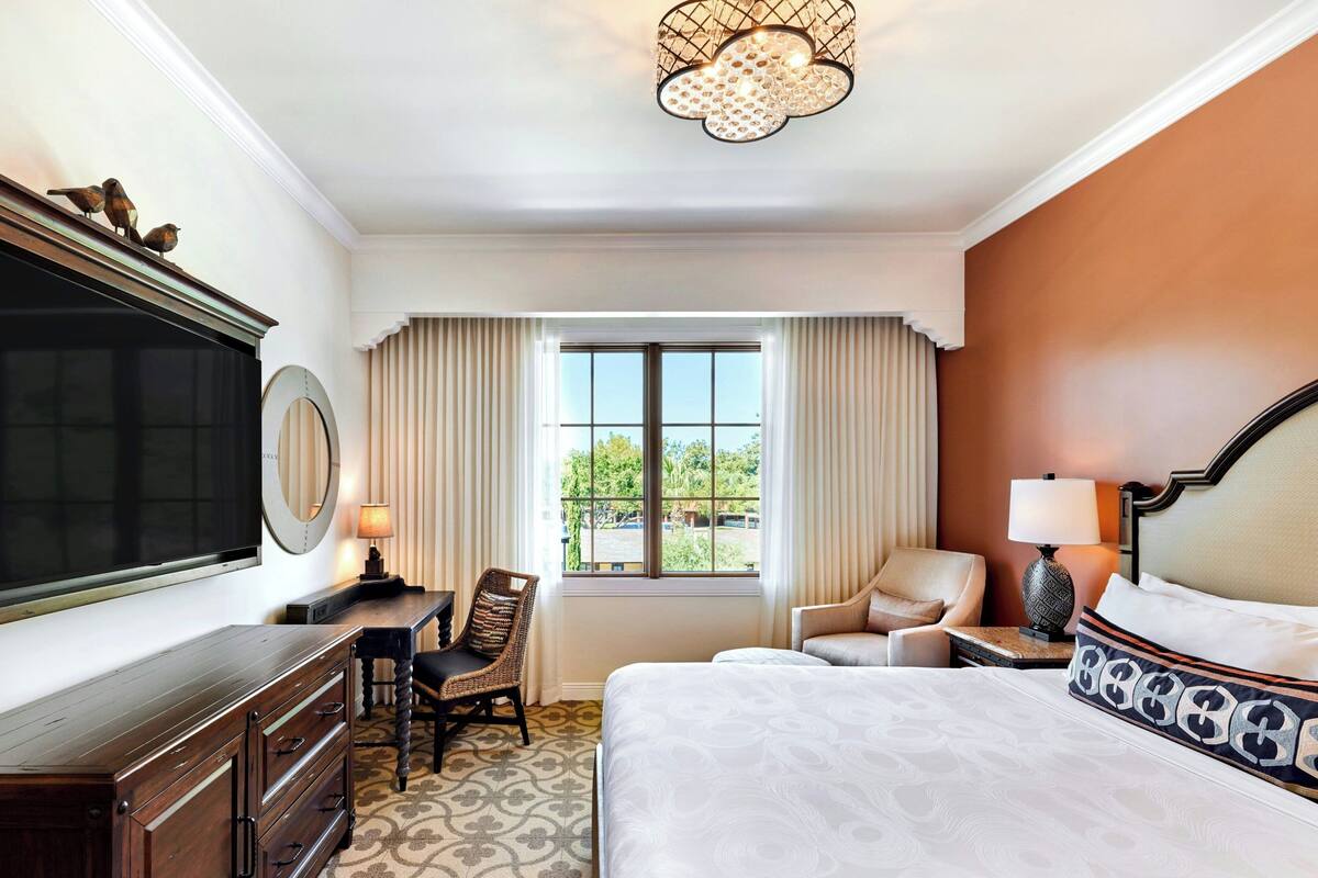 A hotel room with a large bed, a desk with a chair, a television, and a window with curtains.